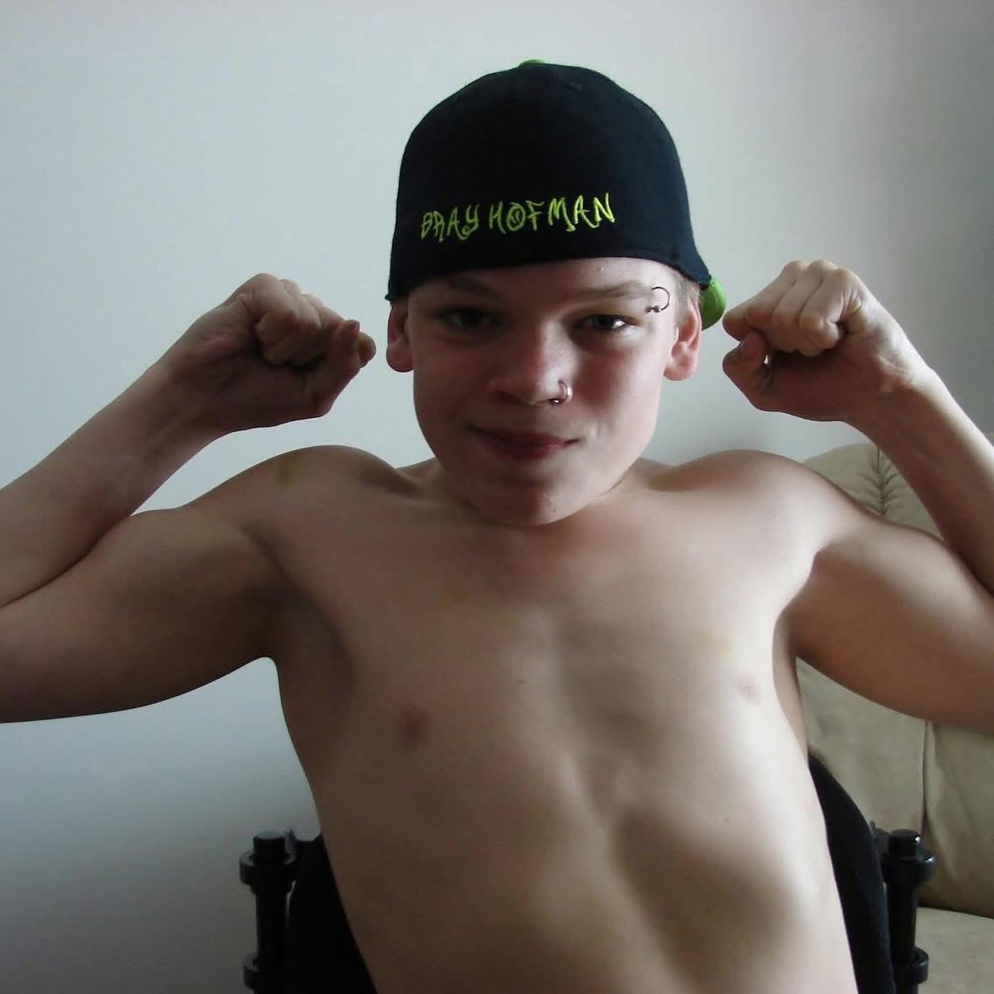 A younger Bray wearing a black baseball cap and flexing both arms.